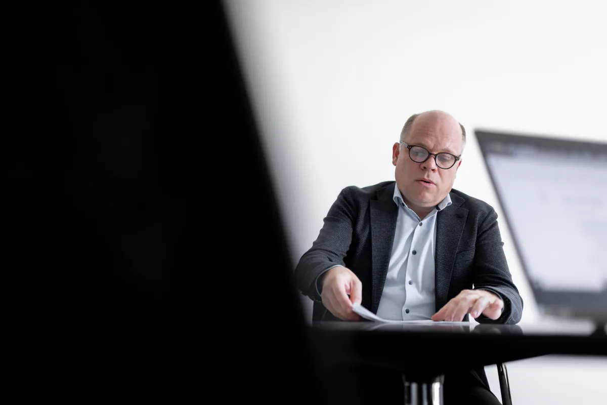 Ein Mann mit Brille sitzt hinter einem Tisch und studiert Unterlagen.